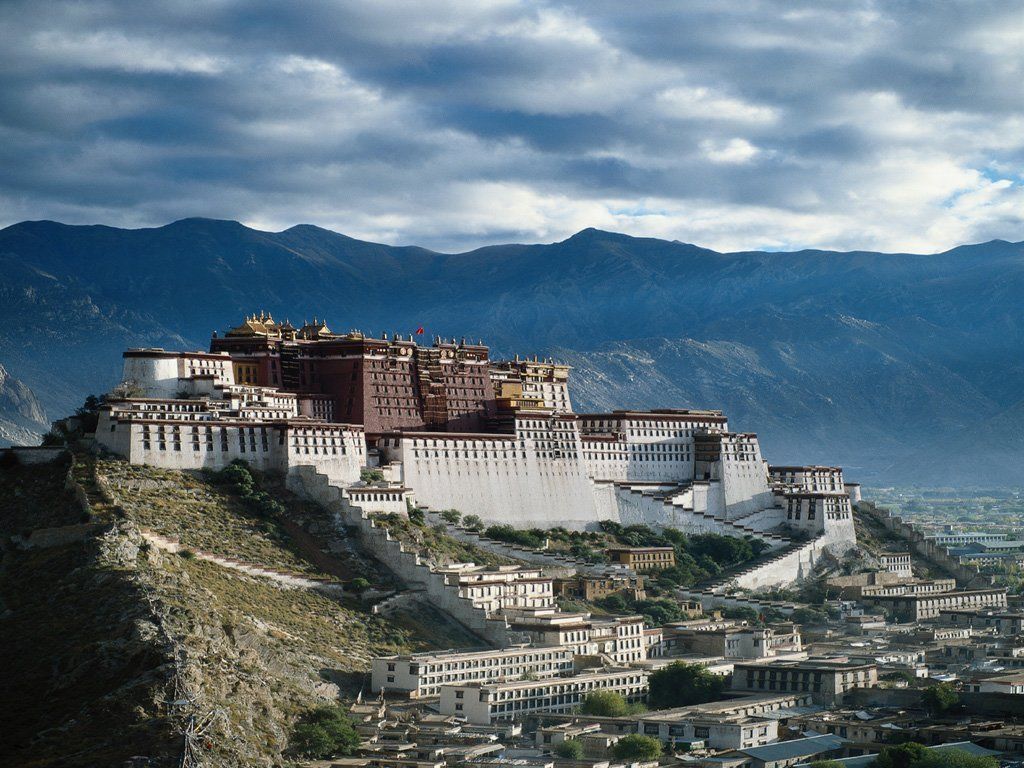 Potala Palace, Lhasa, Tibet, a large white and red fortress on a hillside, with mountains and a blue sky in the background.