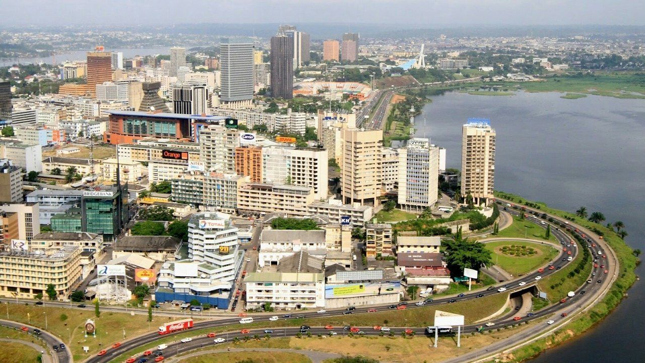 Aerial view of Abidjan, Côte d'Ivoire, a modern city skyline with buildings along a lagoon and a curving highway.