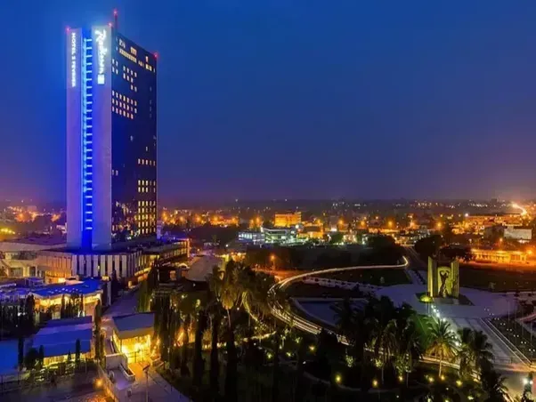 Night view of Accra, Ghana, featuring a lit skyscraper and illuminated cityscape. The sky is dark blue, and city lights create a warm glow.