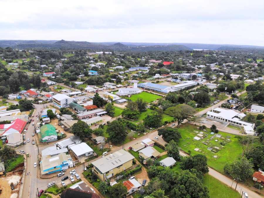 Aerial view of a town with buildings, trees, and a church, set against a backdrop of hills and overcast skies.