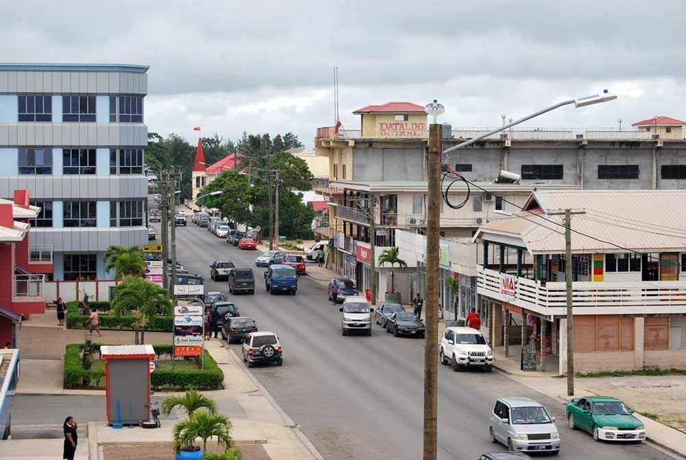 Street scene in a coastal town with cars and buildings, under a cloudy sky.