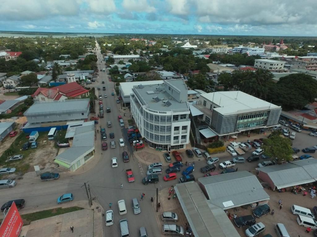 Aerial view of a town with a multistory building on a busy street. Cars, pedestrians, and other buildings are visible under a cloudy sky.
