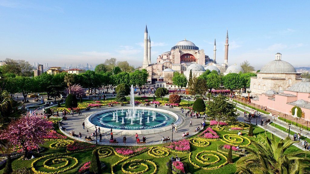 Hagia Sophia in Istanbul, Turkey, seen from a park with a fountain and colorful flowerbeds. Clear blue sky.