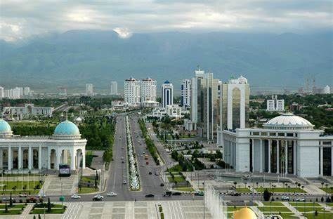 An aerial view of Ashgabat, Turkmenistan, with white buildings lining a wide avenue and mountains in the background.