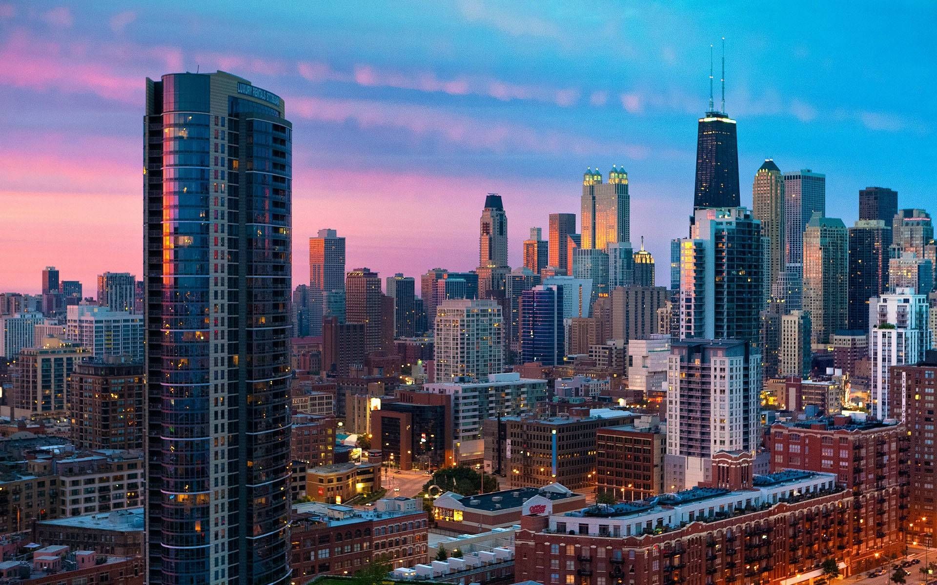 Chicago skyline at dusk, featuring skyscrapers silhouetted against a pink and blue sky.