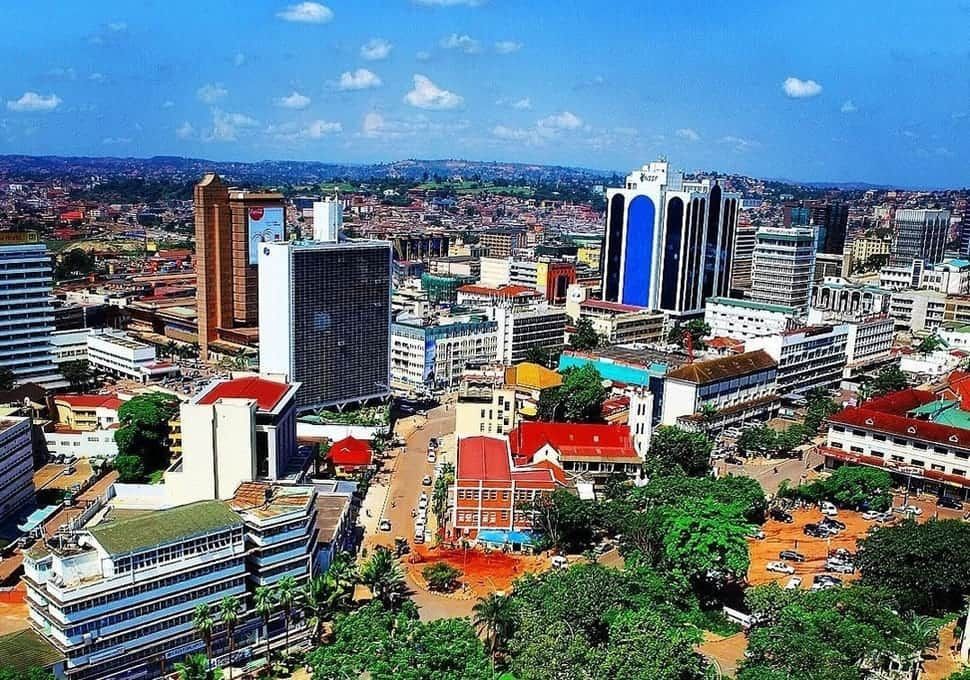 Aerial view of Kampala, Uganda, showing a cityscape with tall buildings, diverse architecture, and a bright blue sky.