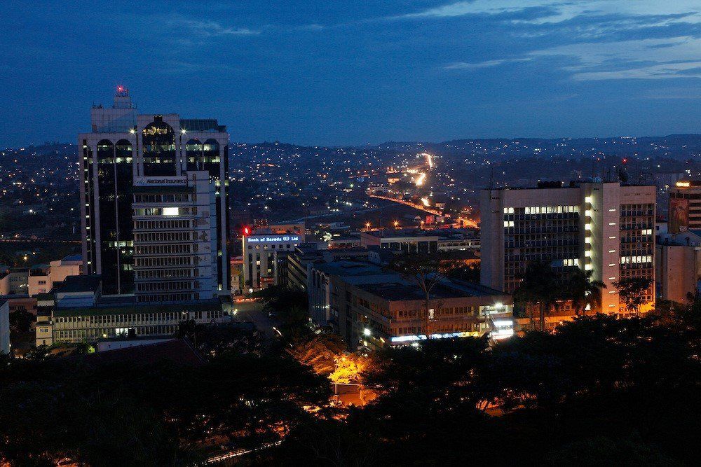 Nighttime cityscape of Kampala, Uganda, with illuminated buildings and lights dotting the distant hills under a dark blue sky.