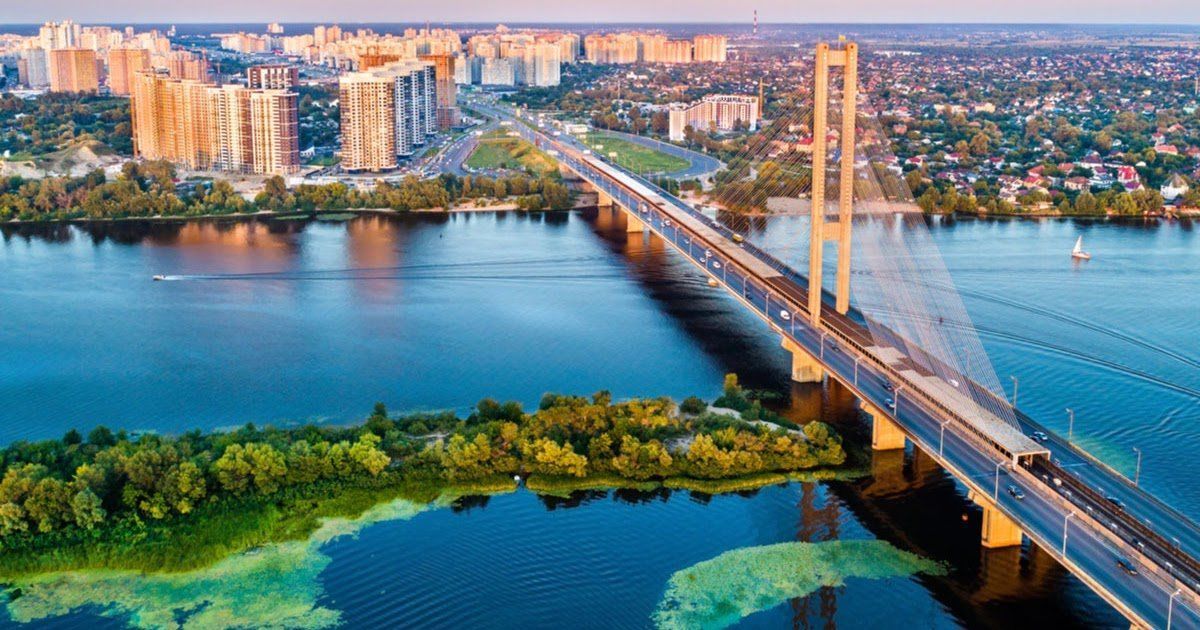 Aerial view of the cable-stayed South Bridge in Kyiv, Ukraine, spanning the Dnipro River, with city buildings in the background.