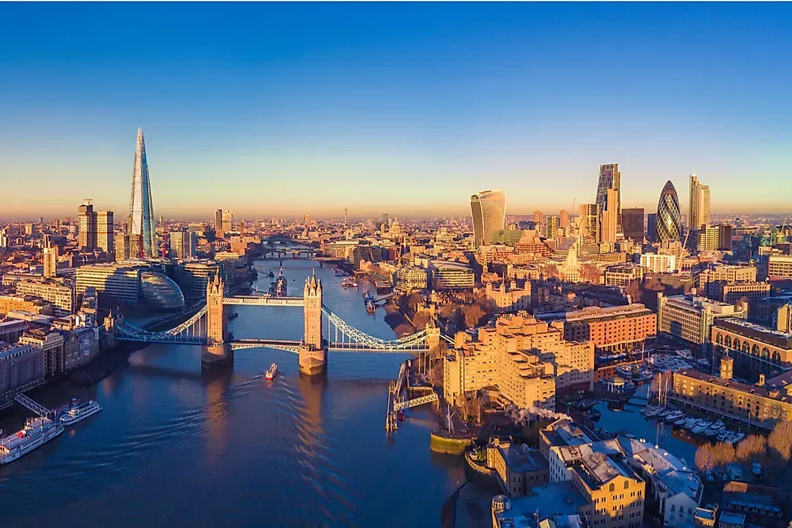 An aerial view of London, showcasing Tower Bridge, the River Thames, and the city skyline with clear blue skies.