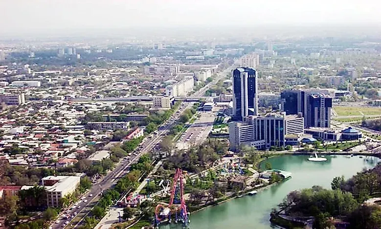 Aerial view of Tashkent, Uzbekistan. A wide boulevard with buildings and a lake in the foreground. Modern high-rise buildings are visible.