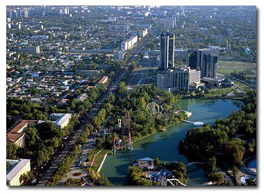 Aerial view of Tashkent, Uzbekistan, featuring a long avenue, high-rise buildings, a lake, and lush greenery.