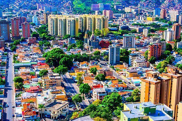 A vibrant aerial view of Caracas, Venezuela, with colorful buildings, lush greenery, and mountains in the background.