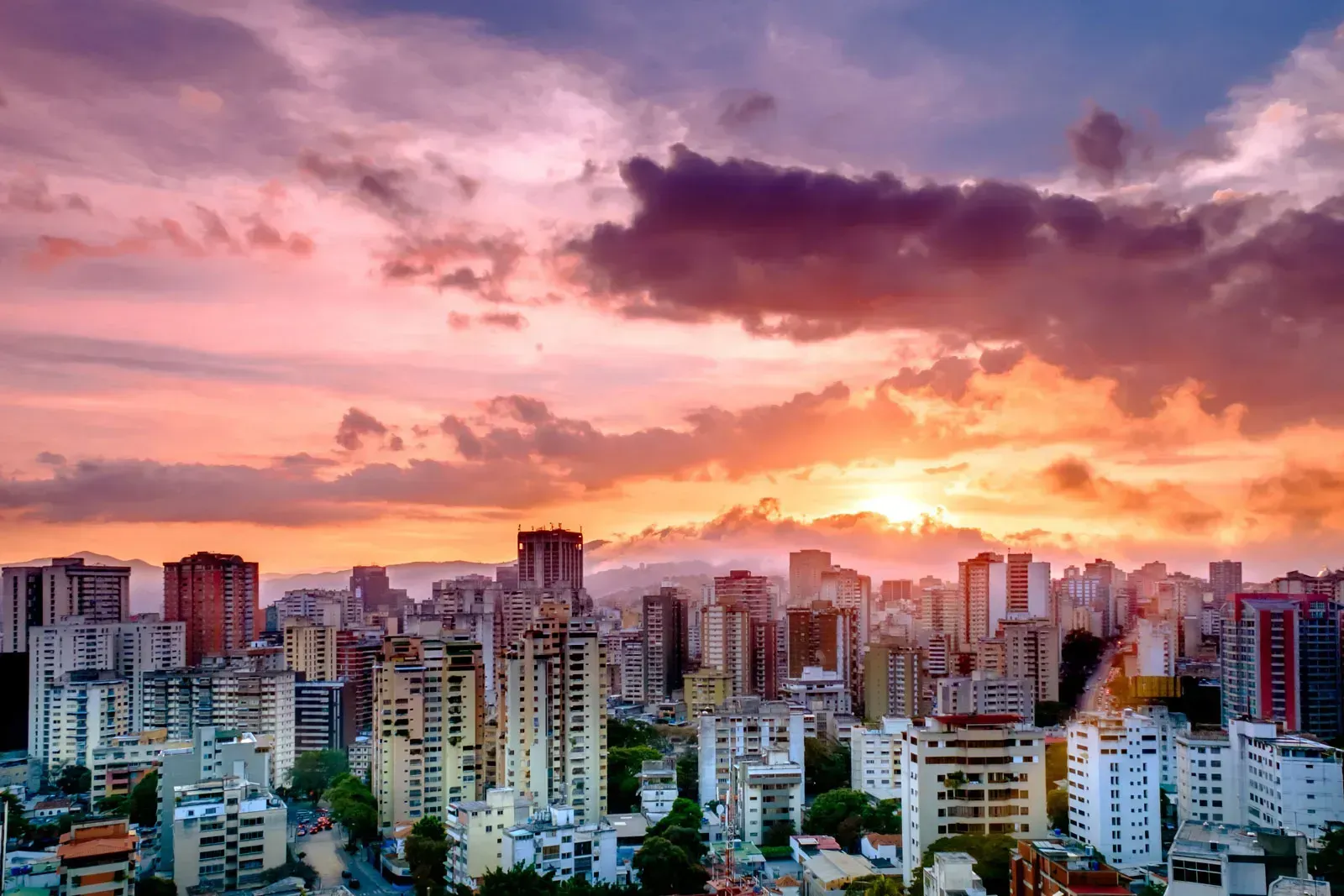 City skyline at sunset with a colorful sky of orange, pink, and purple hues; buildings in silhouette.