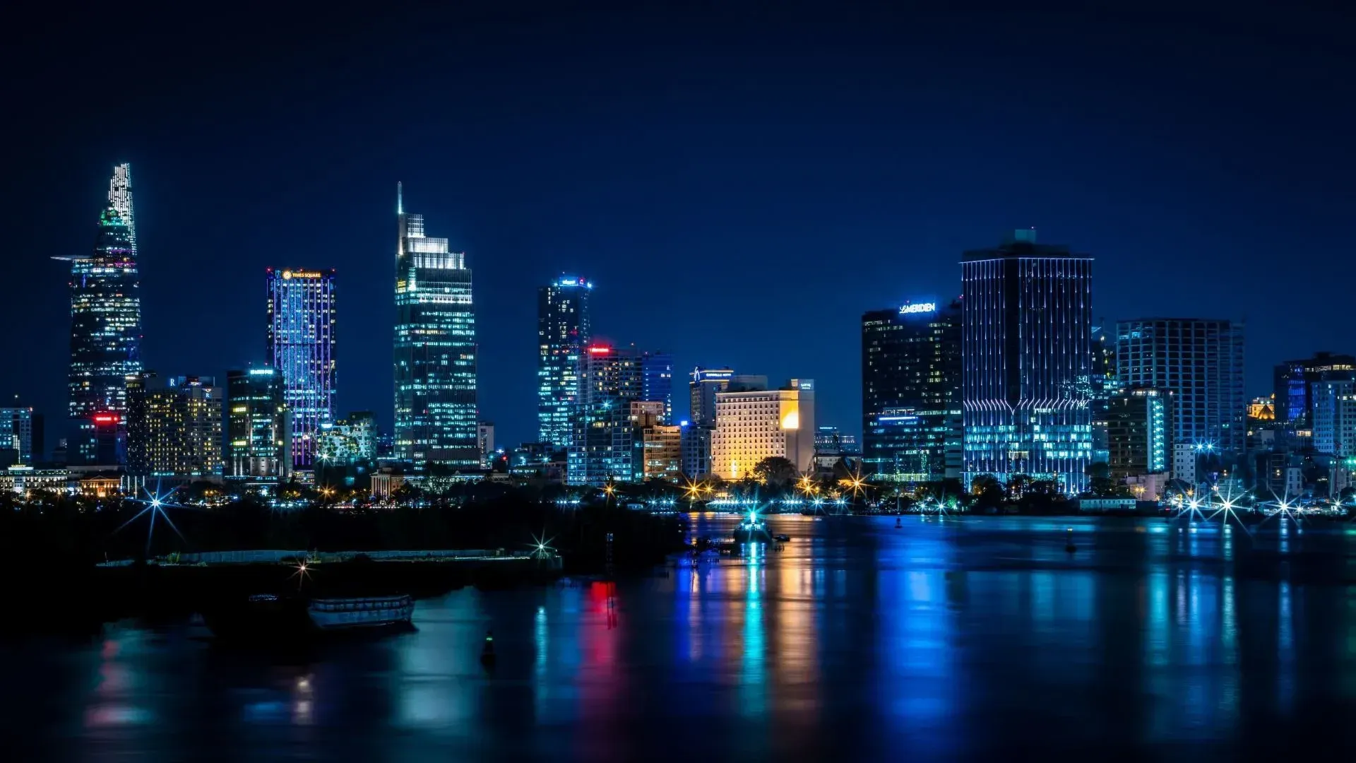 Nighttime skyline of Ho Chi Minh City, Vietnam, illuminated with colorful lights reflecting on the water.