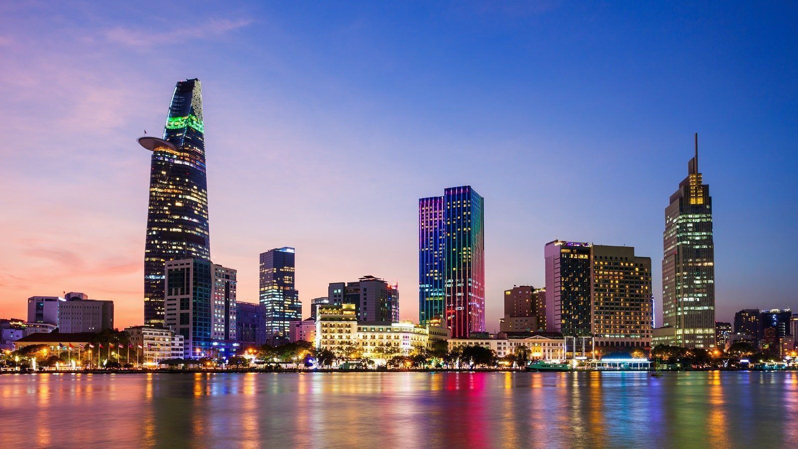 Skyline of Ho Chi Minh City, Vietnam at dusk. Modern skyscrapers illuminated against a colorful sky reflected in the water.