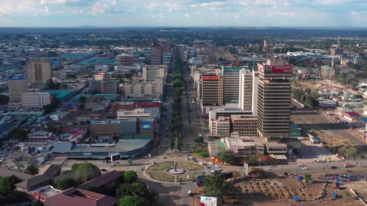 Aerial view of Lusaka, Zambia. A wide avenue lined with buildings stretches toward the horizon under a bright, sunny sky.