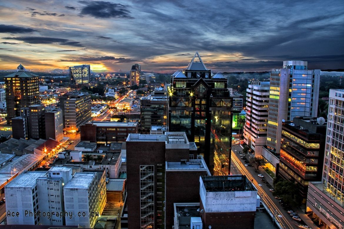 City skyline at dusk, illuminated by streetlights against a dark blue and orange sky.
