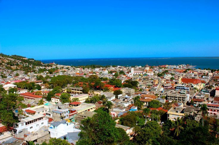 Aerial view of a coastal city with buildings, trees, and the ocean under a clear blue sky.