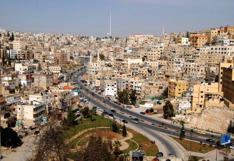 Amman, Jordan cityscape with tan buildings, a highway, and a tall antenna tower under a blue sky.