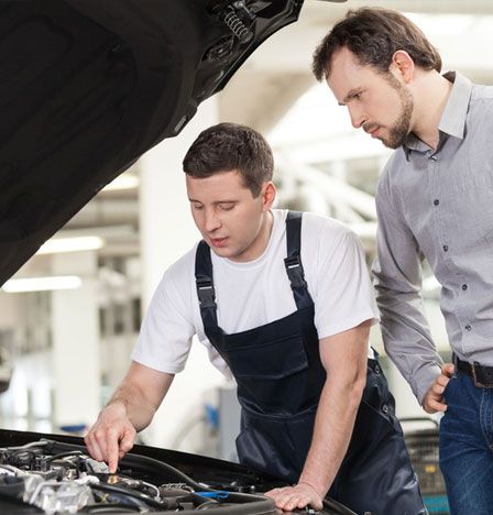 An auto mechanic repairing the car engine with a customer beside him