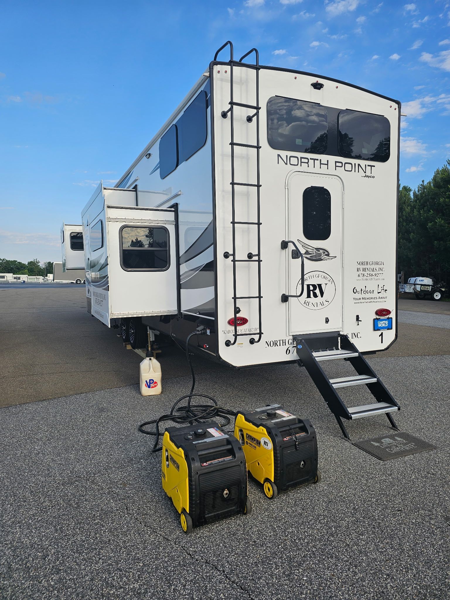 A large white RV parked on gravel with two yellow generators in front.