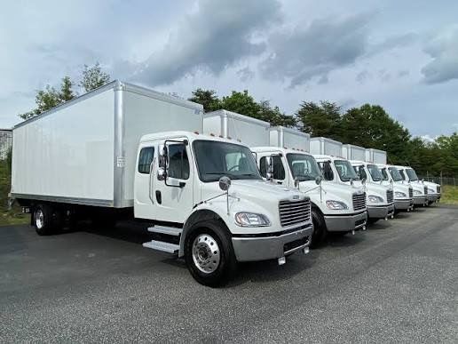 White box trucks lined up on asphalt under a cloudy sky