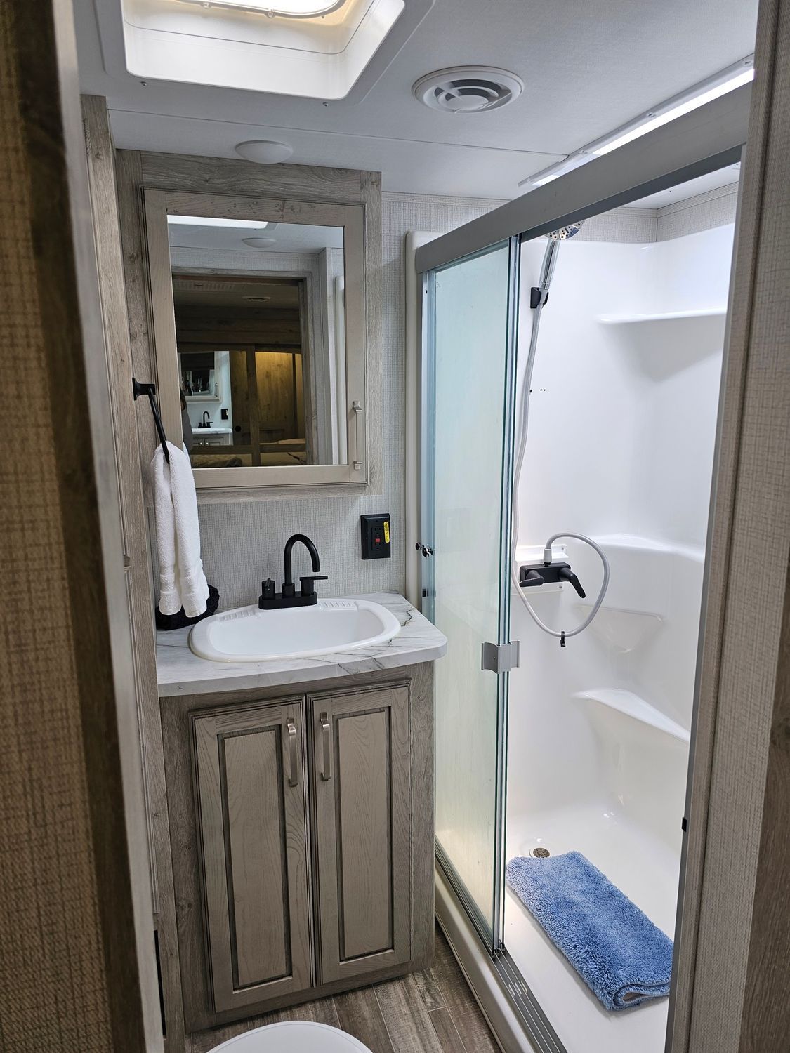 RV bathroom with vanity, sink, shower, and blue bathmat.