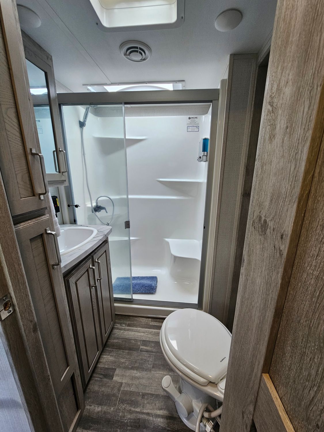 RV bathroom with toilet, shower, sink, and cabinets. Gray and white interior.
