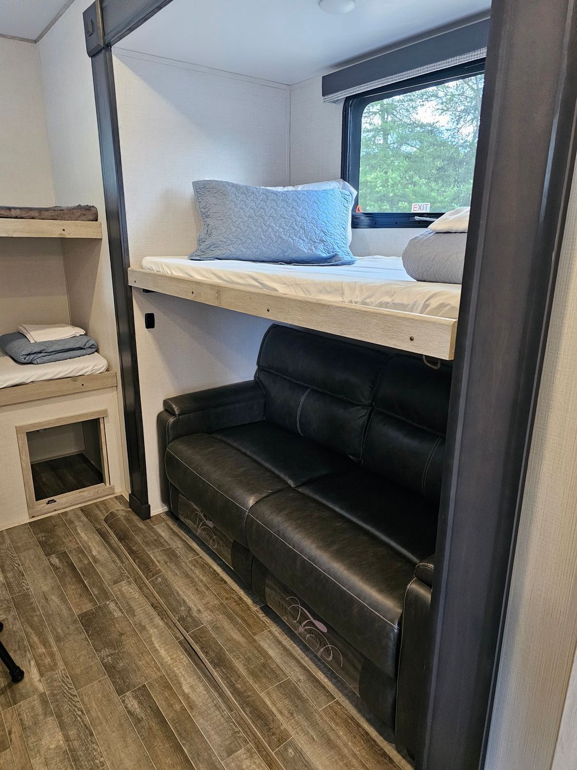 RV interior with bunk bed over black leather sofa, window to the right.