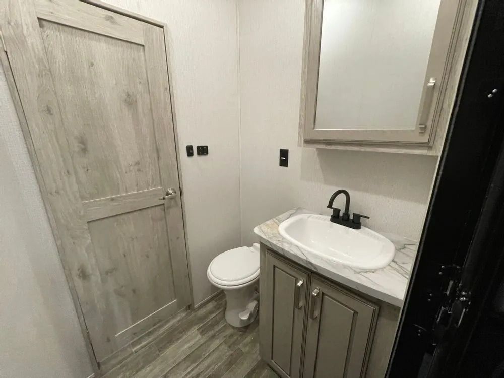 RV bathroom with toilet, sink, vanity, mirror, and closed door.