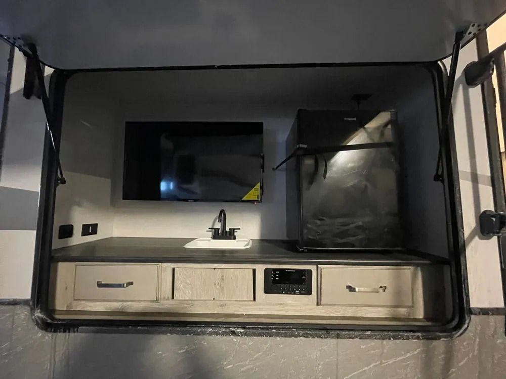 Outdoor RV kitchen with TV, sink, refrigerator, and storage.