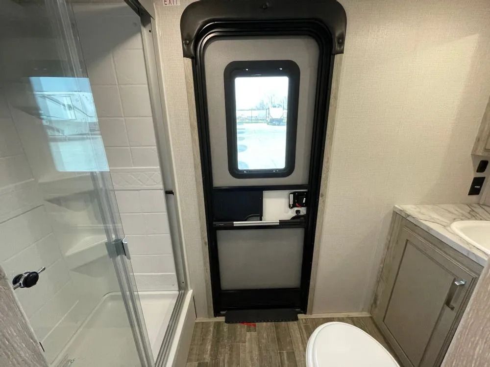 Bathroom with shower, toilet, and RV door. Gray and beige color scheme