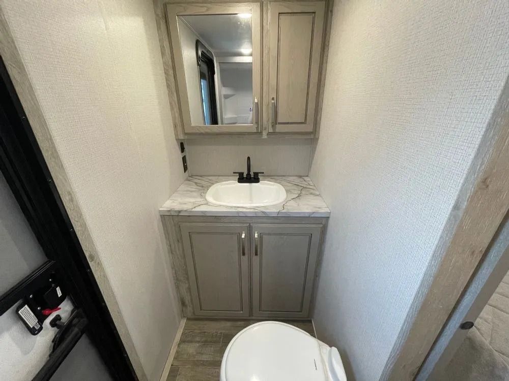 RV bathroom with sink, vanity, mirror, and toilet; gray cabinets and countertops.