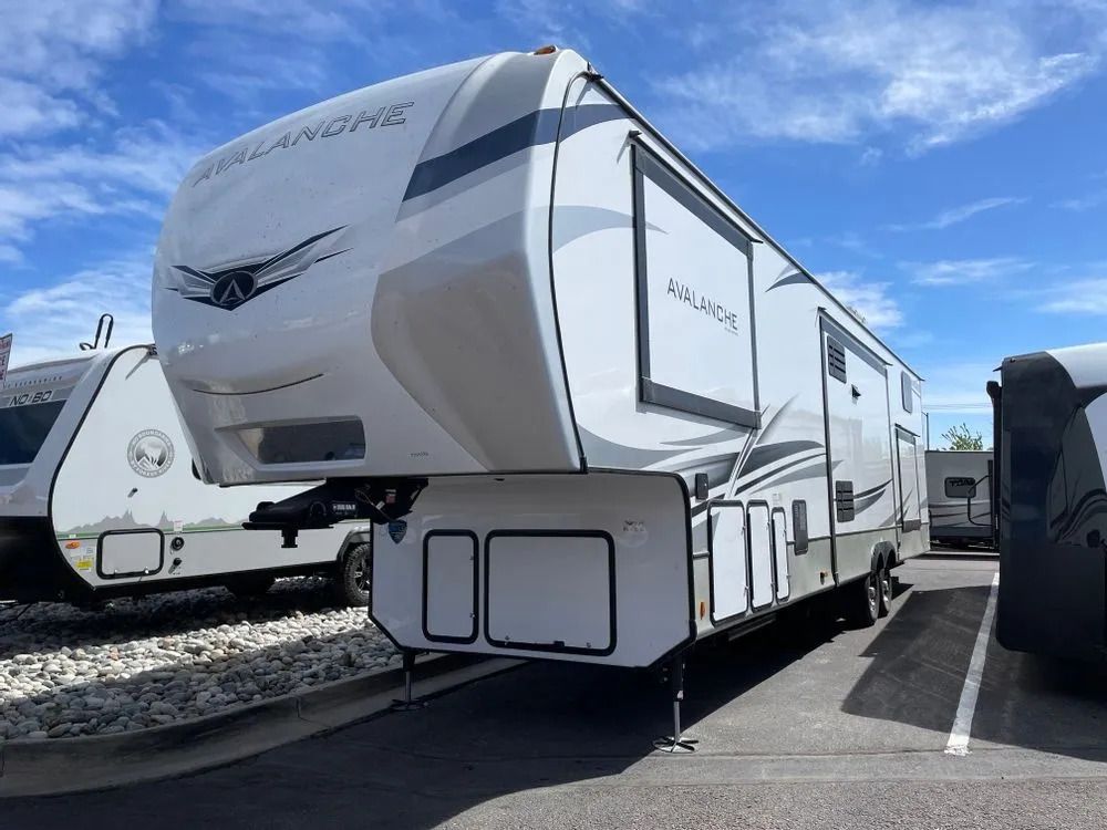 White and grey Avalanche fifth wheel RV parked outside on a sunny day