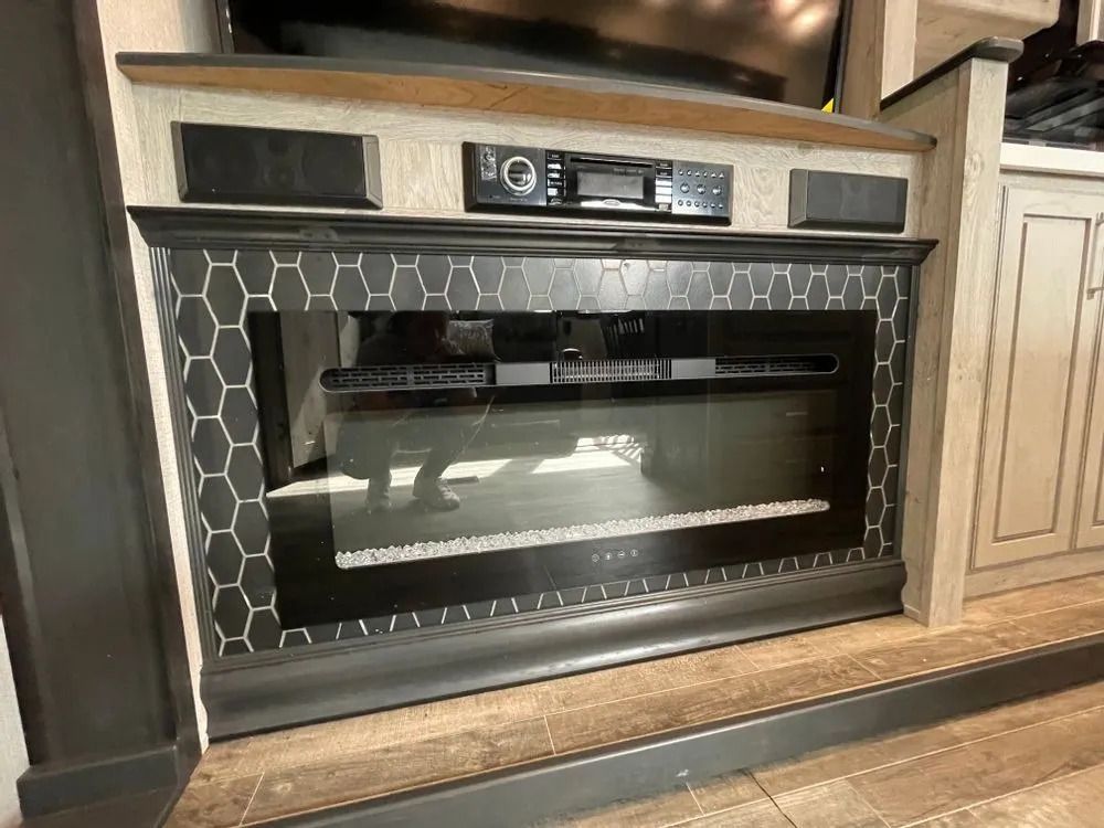 Fireplace with black and white hexagon tile surround, speakers, and entertainment system in a camper