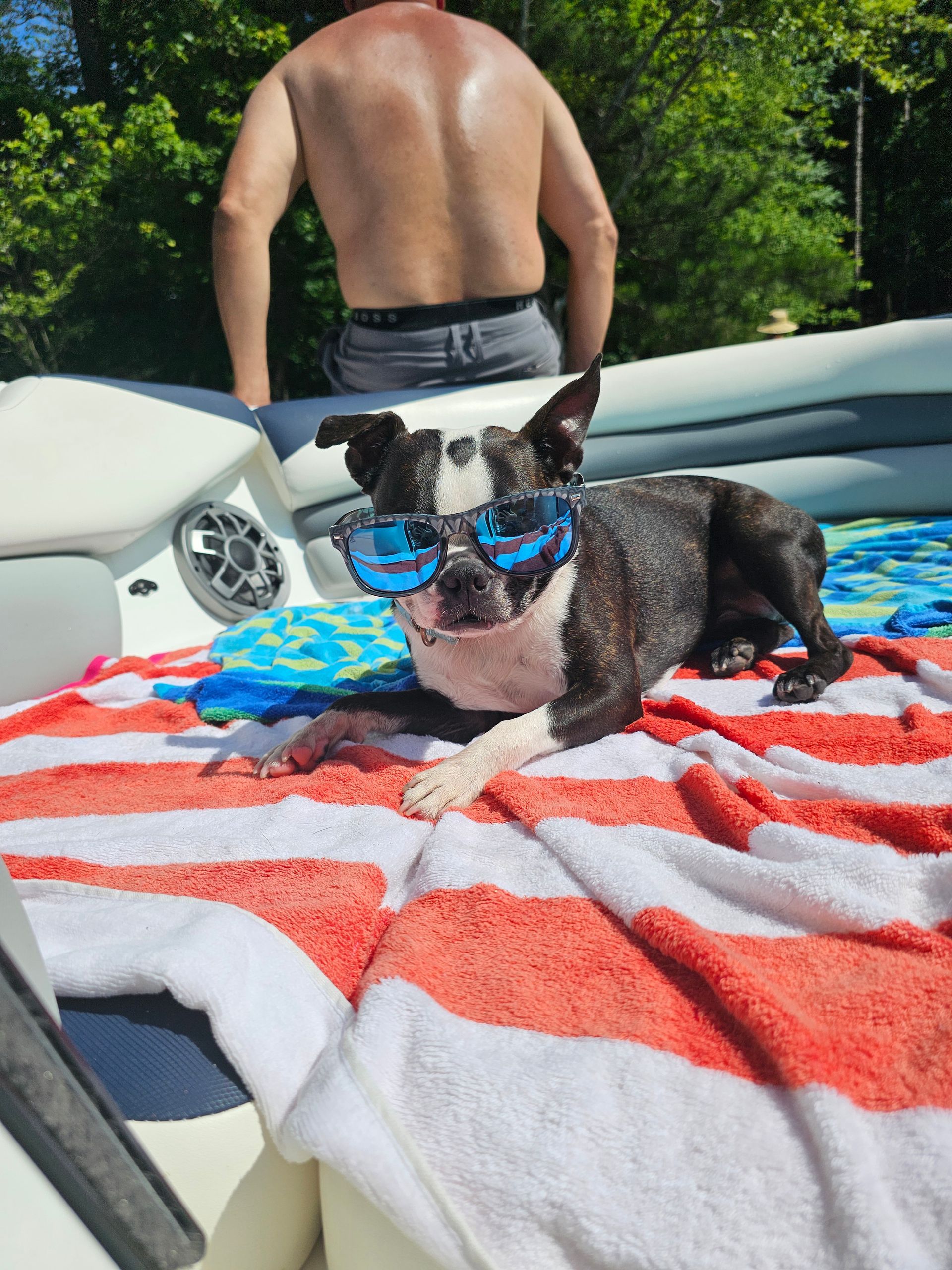 A dog wearing sunglasses is laying on a striped towel on a boat.