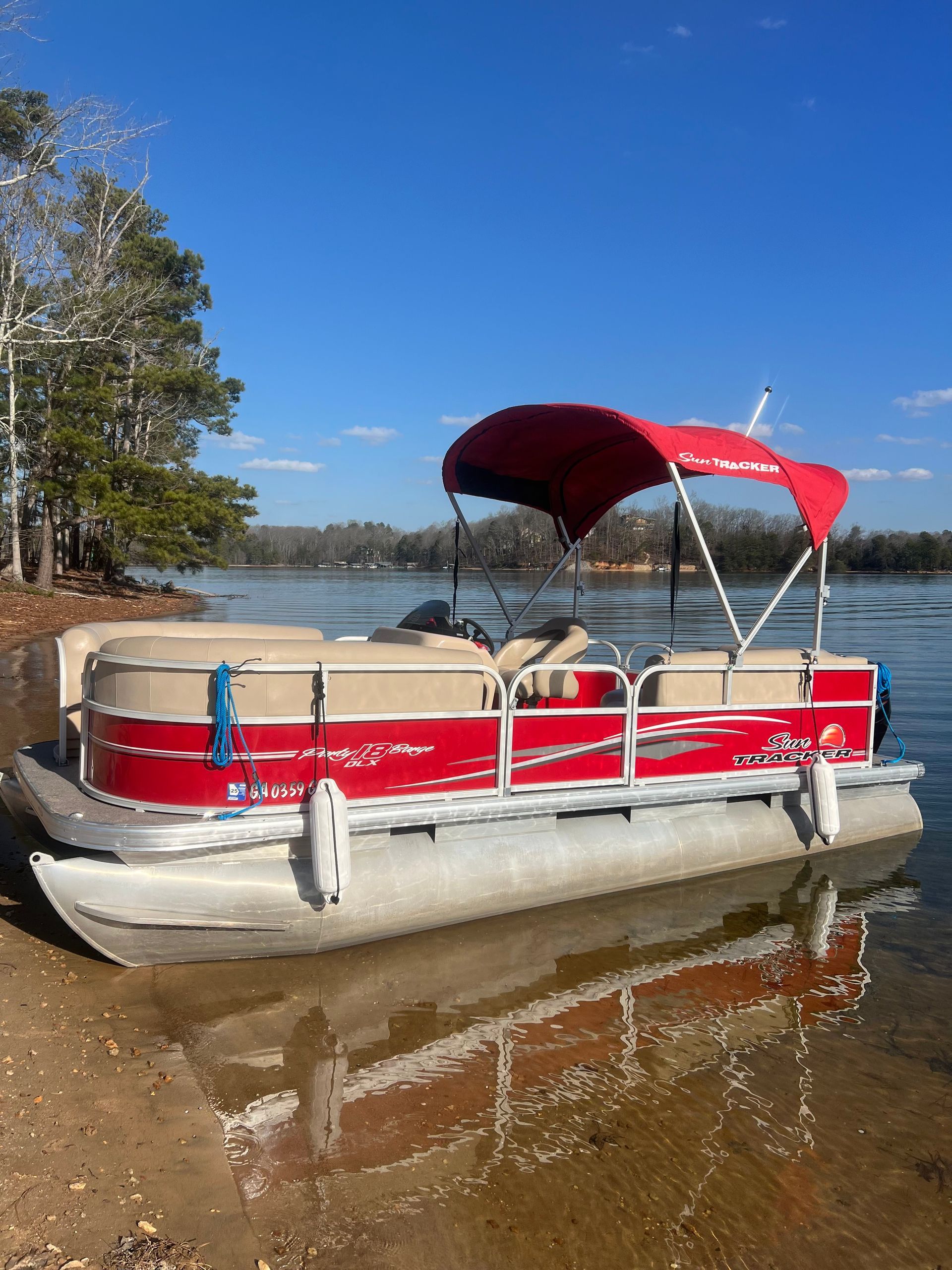 A red pontoon boat is docked on the shore of a lake.