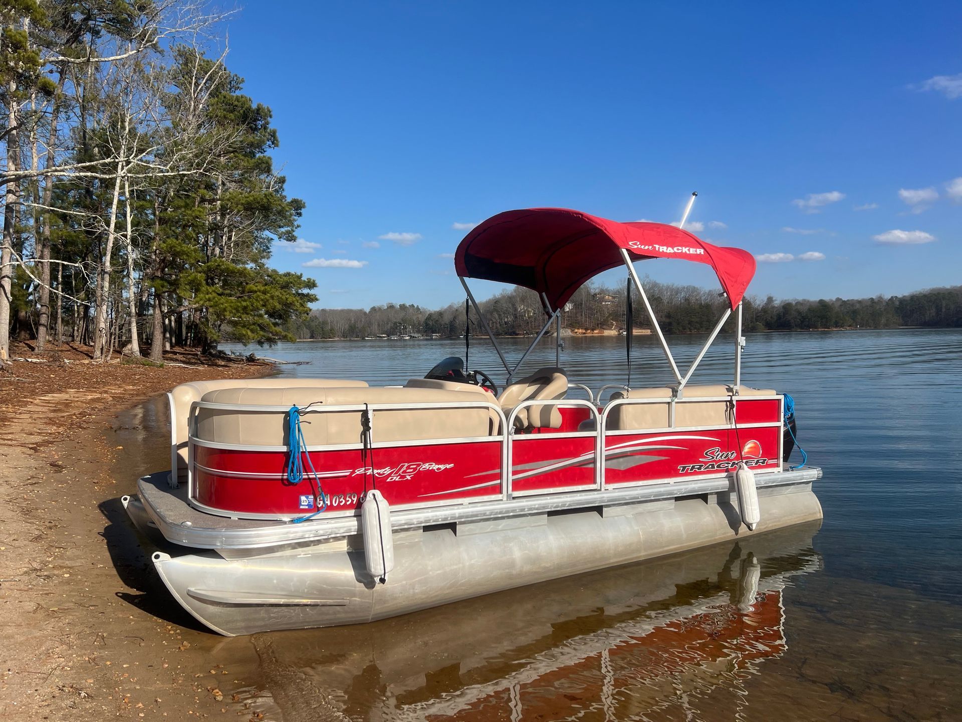 A red pontoon boat with a red canopy is docked on the shore of a lake.