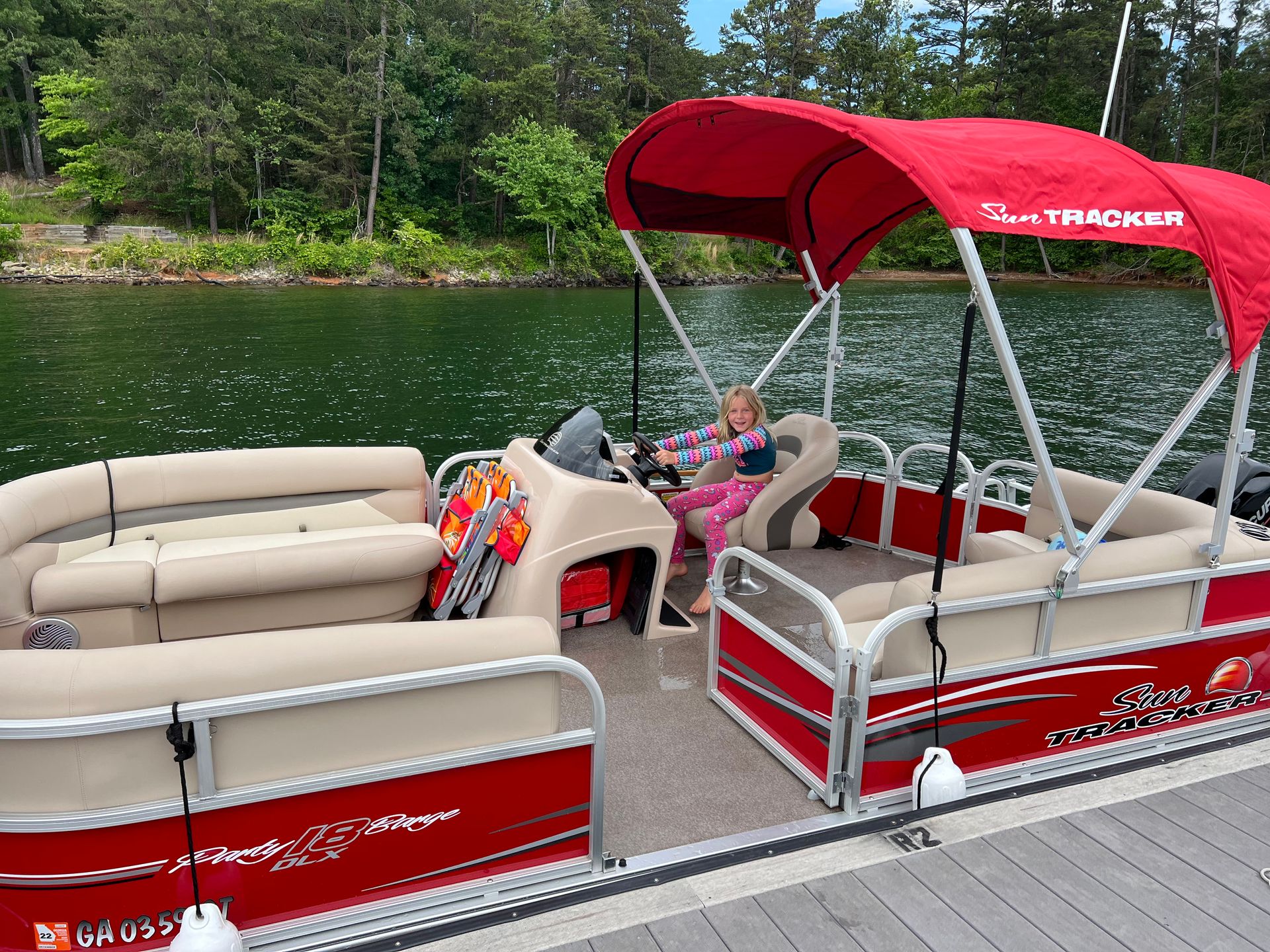 A red and white pontoon boat is parked on the shore of a lake.