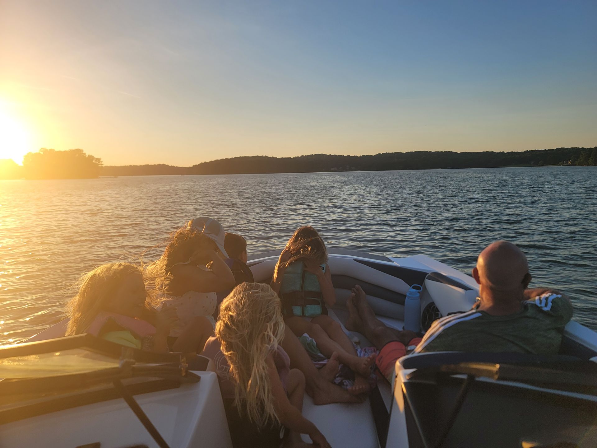 A group of people are sitting on the back of a boat on a lake.