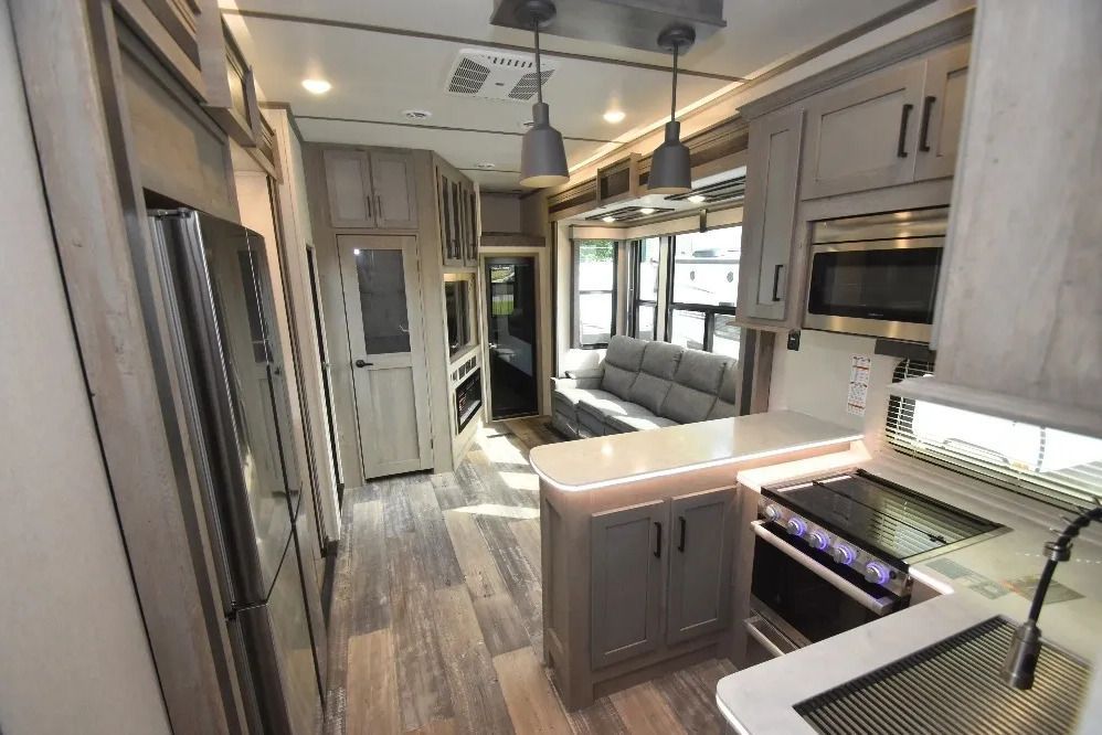 A kitchen with a stove, refrigerator, microwave and a couch.