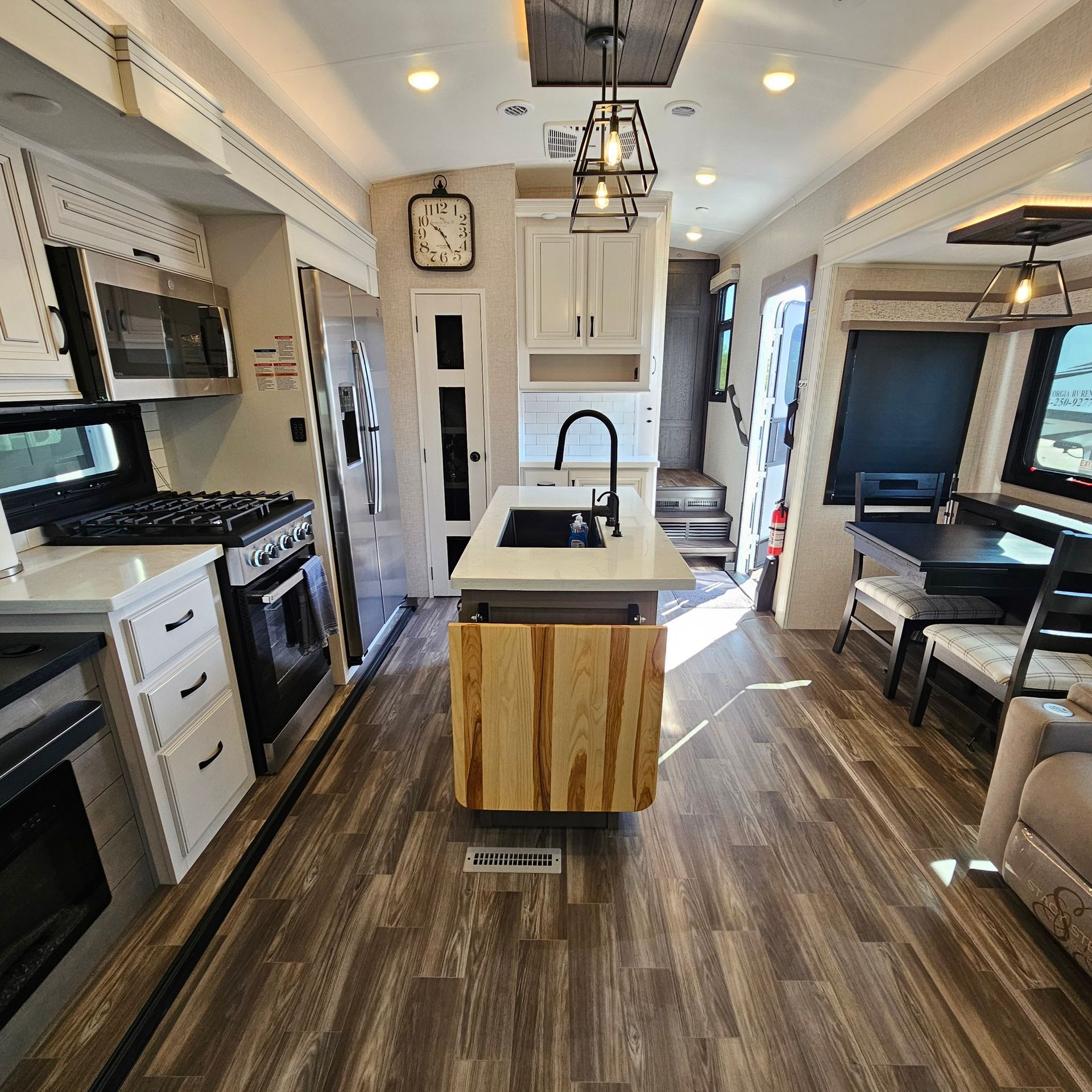 Interior of a modern RV kitchen with white cabinets, wood island, and stainless steel appliances