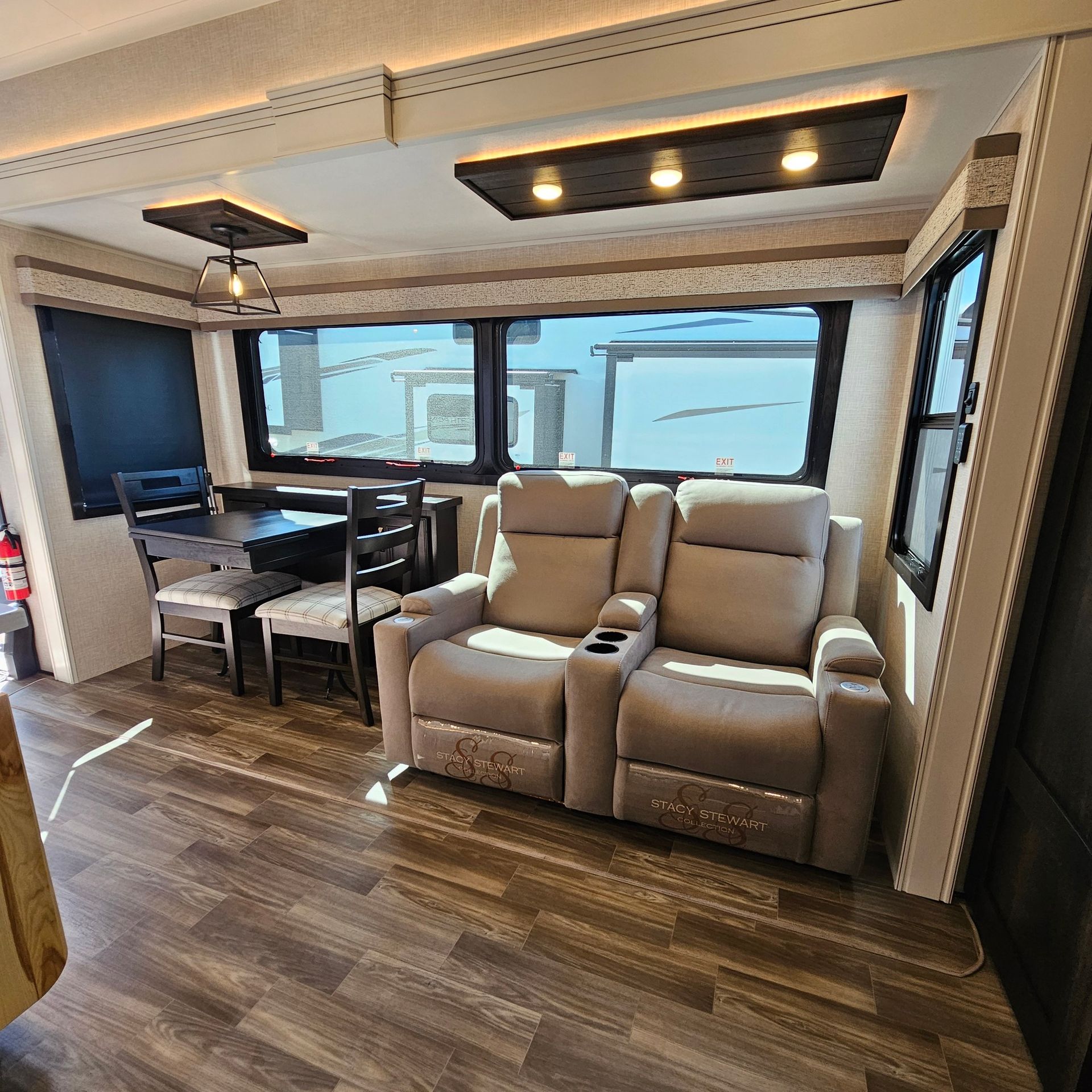 Interior of an RV with a dining area, recliner seats, and windows. Wooden floors and neutral color scheme