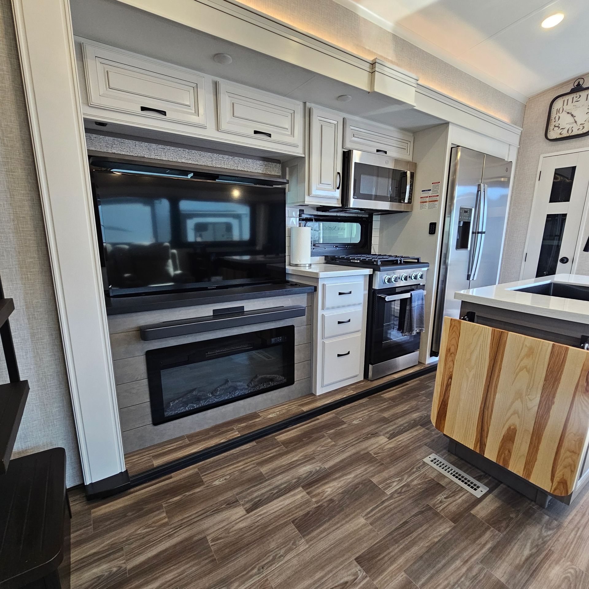 Interior of a modern RV kitchen featuring a stove, microwave, refrigerator, and fireplace