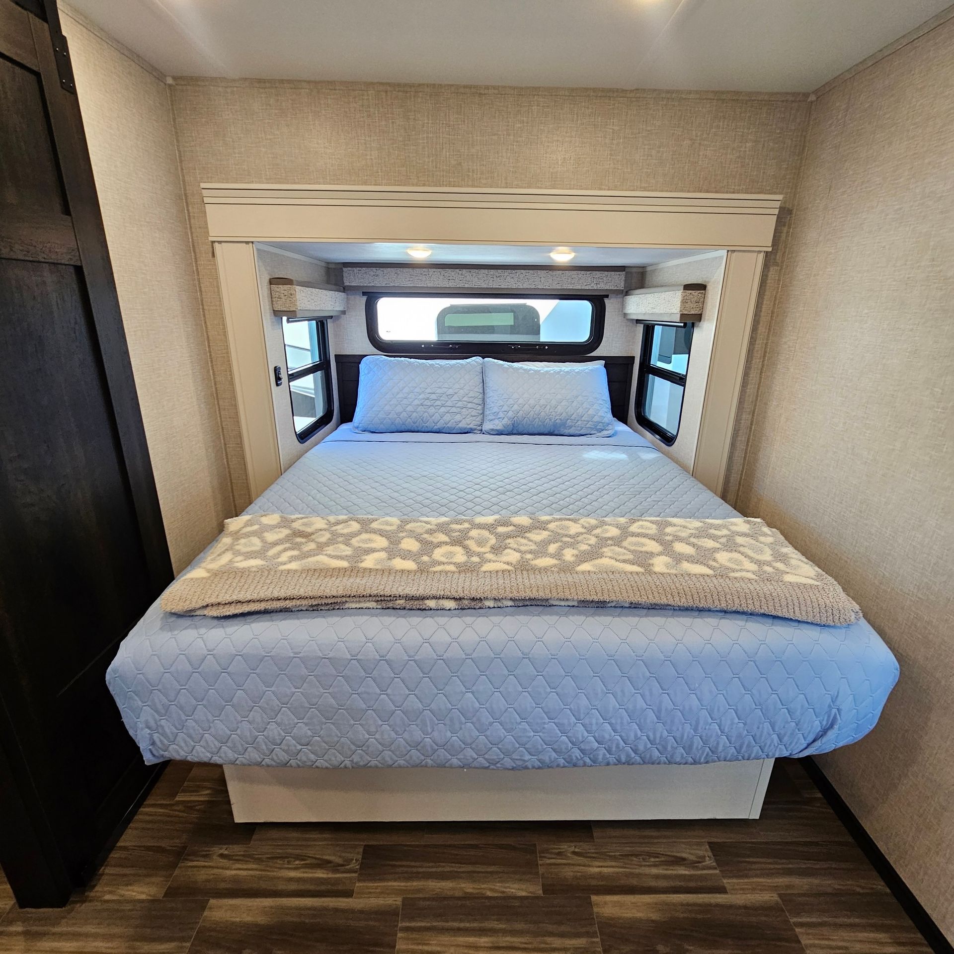 Bedroom in a RV with a bed, blue bedding, and overhead cabinets