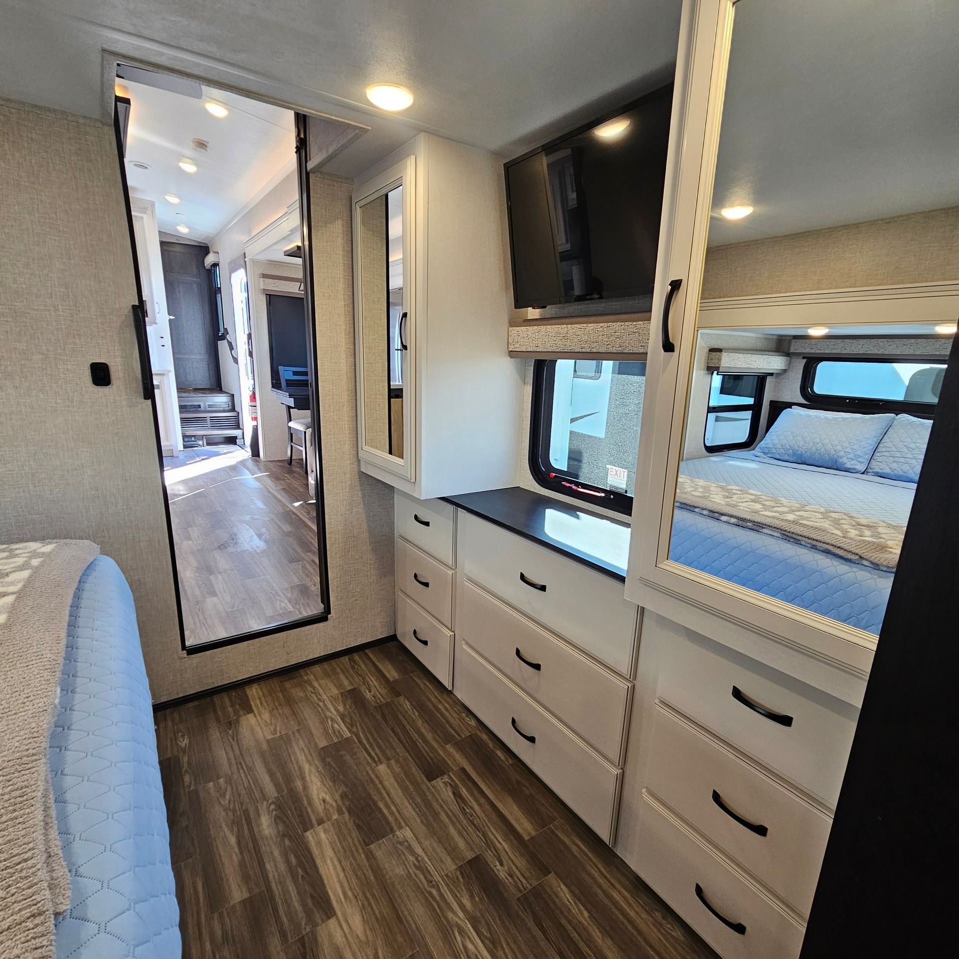 Interior of a camper bedroom featuring a full-length mirror, dresser, tv, and bed