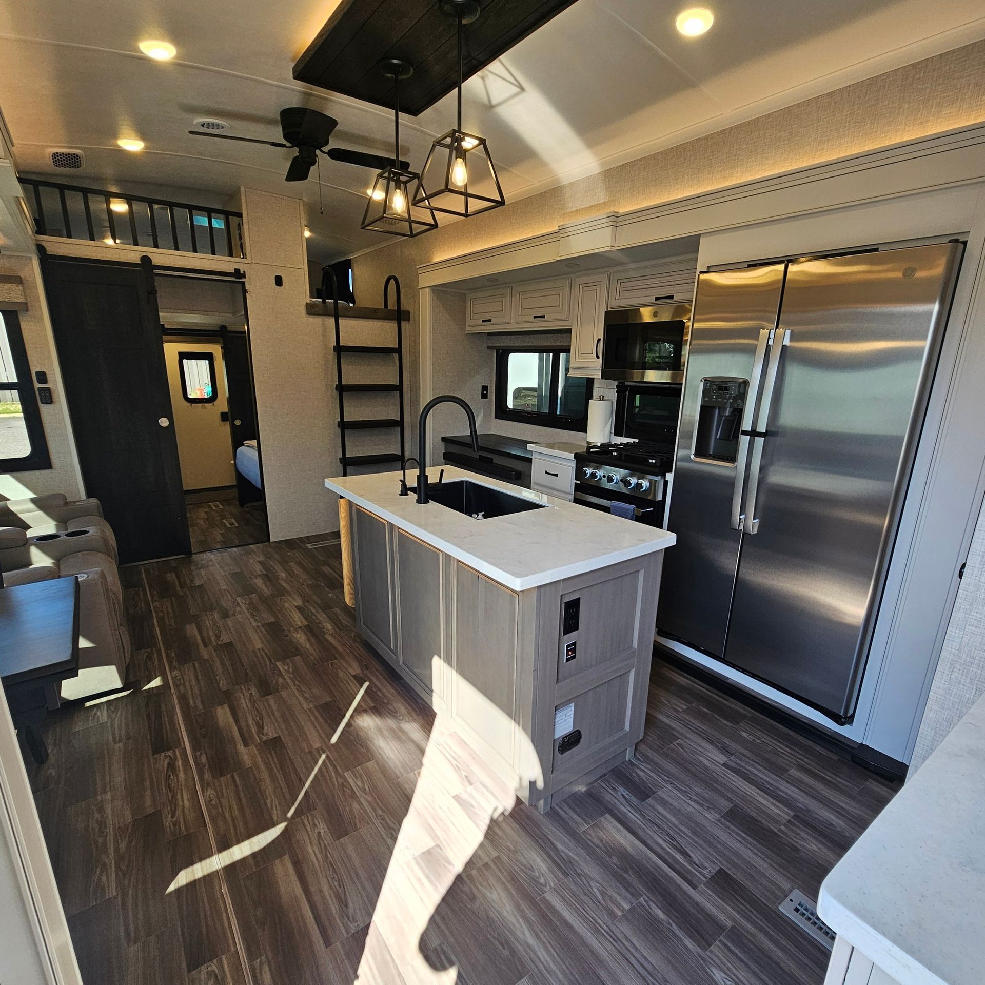 Interior of a modern RV kitchen with white cabinets, wood island, and stainless steel appliances