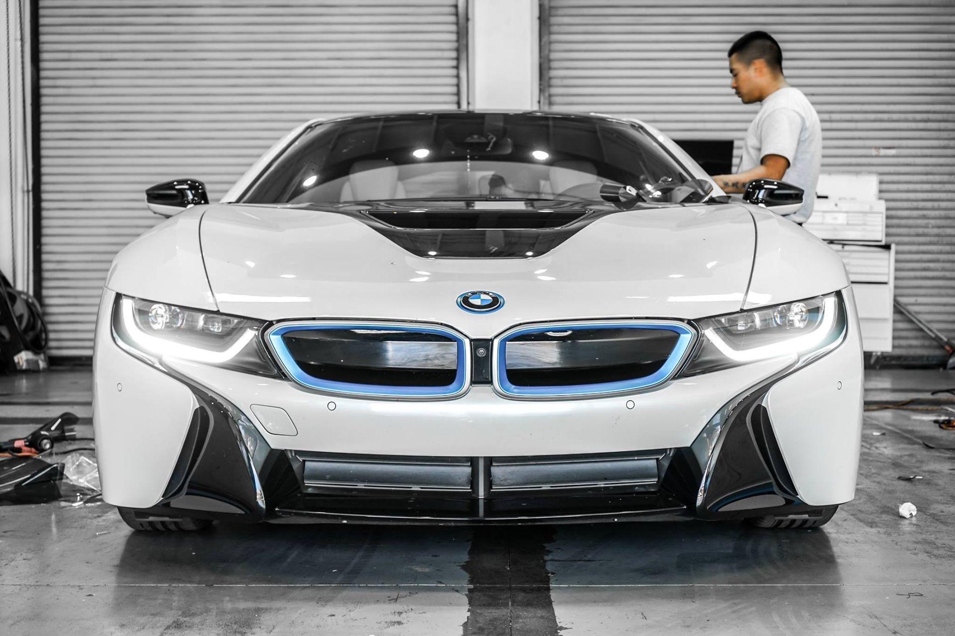 White BMW i8 car in a garage with a person working on the hood.