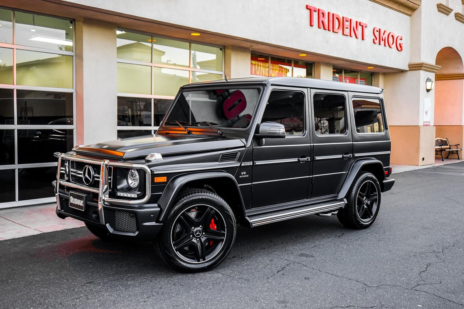 Dark gray Mercedes-Benz G-Class SUV parked in front of a store with a red sign that says 