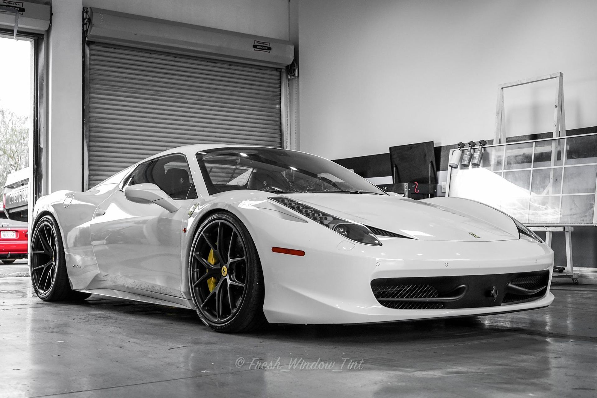 White Ferrari 458 Italia sports car in a garage with black rims and yellow brake calipers.